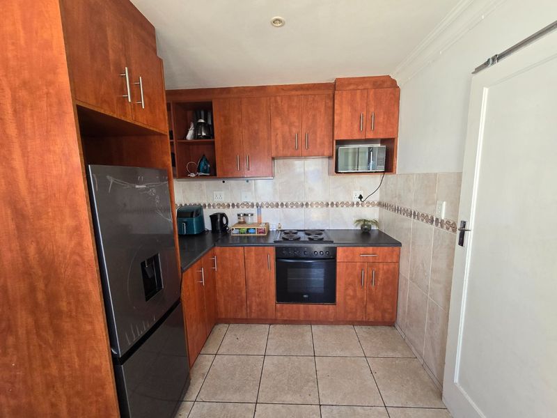 A functional kitchen featuring wooden cabinetry, laminate countertops, a built-in oven with electric hob, and tiled flooring.