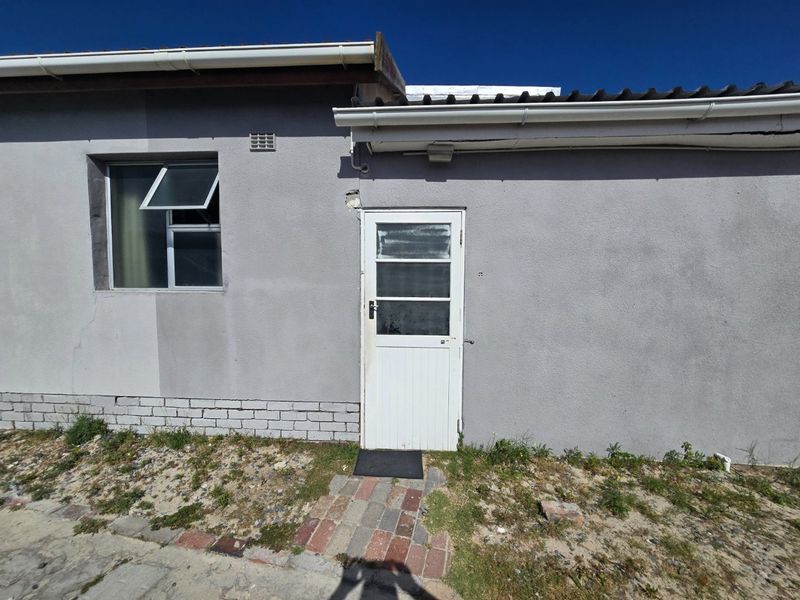 Rear exterior view of the property featuring plastered walls, a timber door, and an aluminium window frame with visible signs of wear.