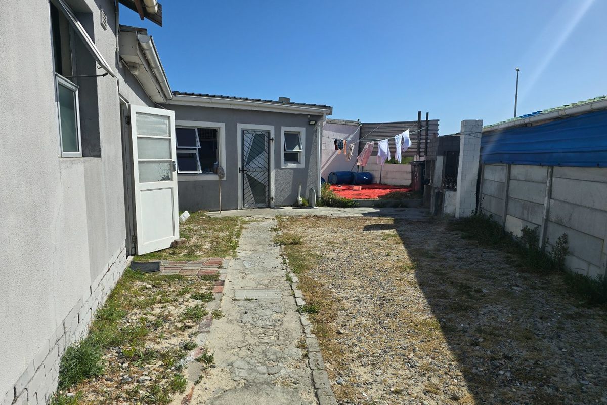 Rear exterior view of the property featuring a concrete pathway, security gate, and perimeter walling, with potential for landscaping improvements.