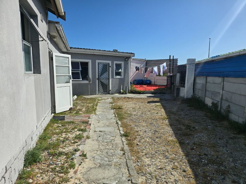 Rear exterior view of the property featuring a concrete pathway, security gate, and perimeter walling, with potential for landscaping improvements.