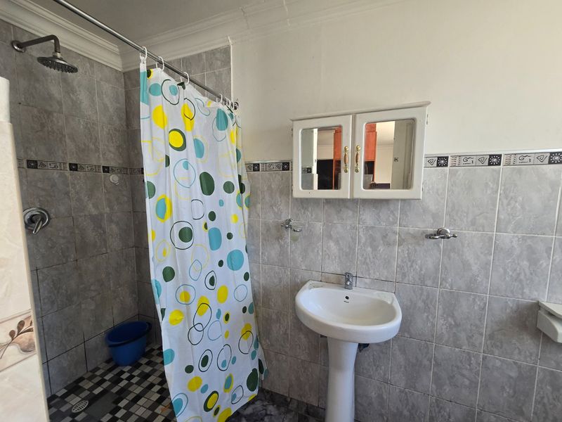 A functional bathroom featuring a pedestal sink, wall-mounted medicine cabinet, and a shower area with tiled walls and flooring.