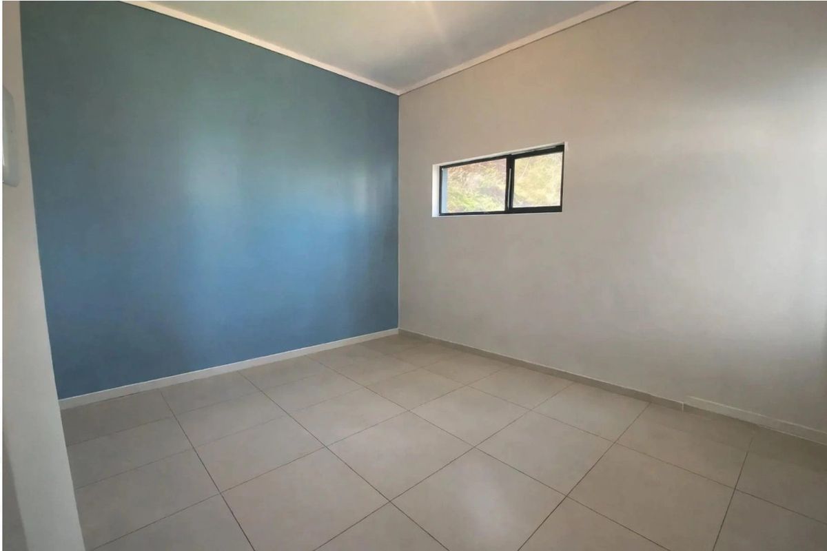A clean, empty bedroom featuring neutral tiled flooring and a modern blue accent wall with a small aluminium-framed window.