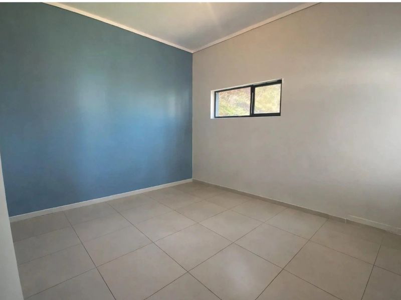 A clean, empty bedroom featuring neutral tiled flooring and a modern blue accent wall with a small aluminium-framed window.