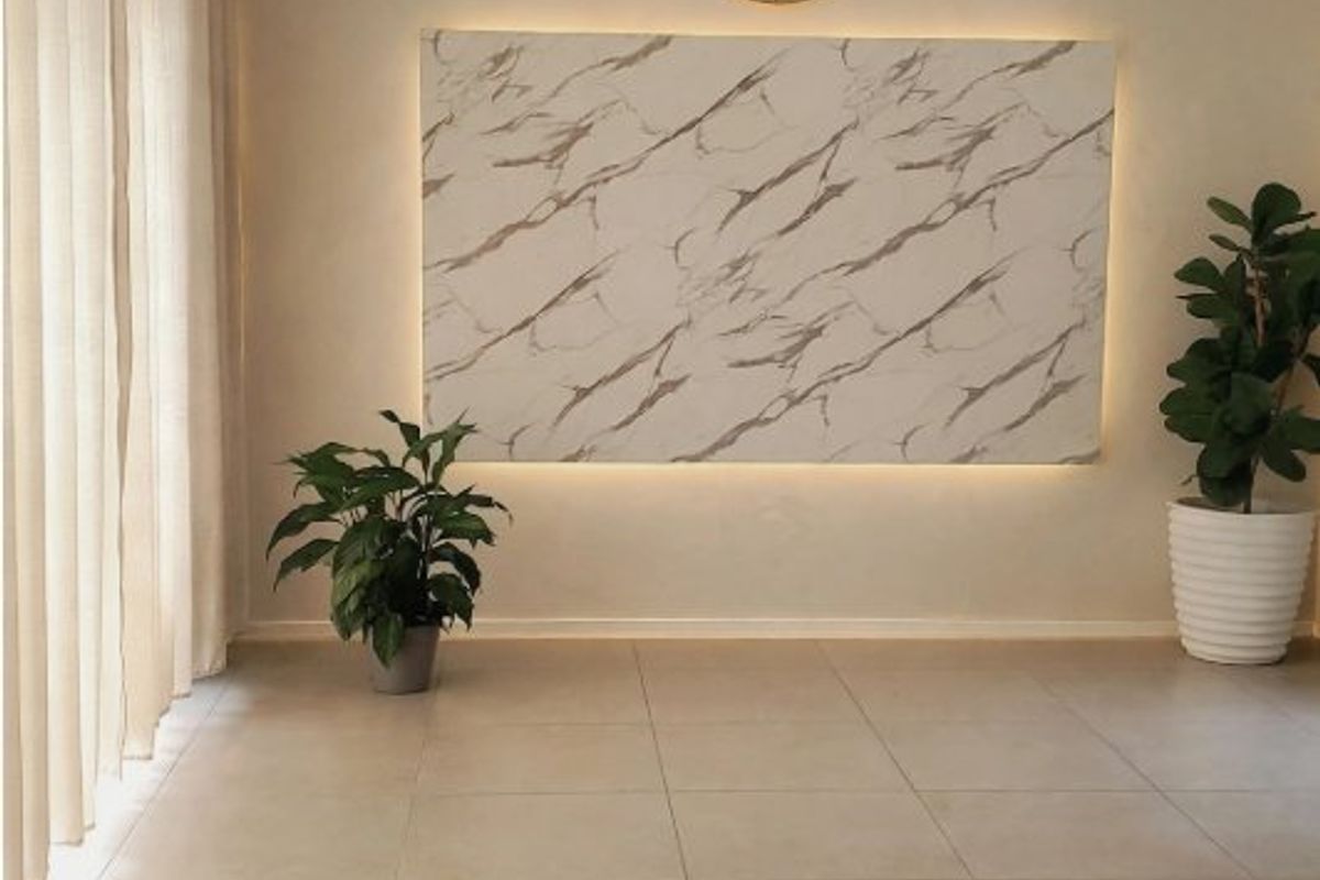 A bright, modern living area featuring large format floor tiles, a backlit marble-effect feature wall, and contemporary track lighting.