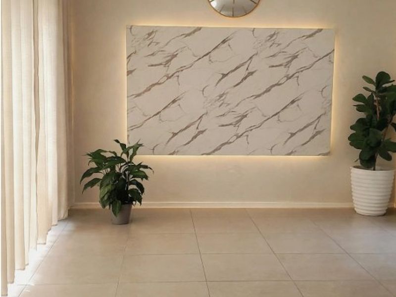 A bright, modern living area featuring large format floor tiles, a backlit marble-effect feature wall, and contemporary track lighting.