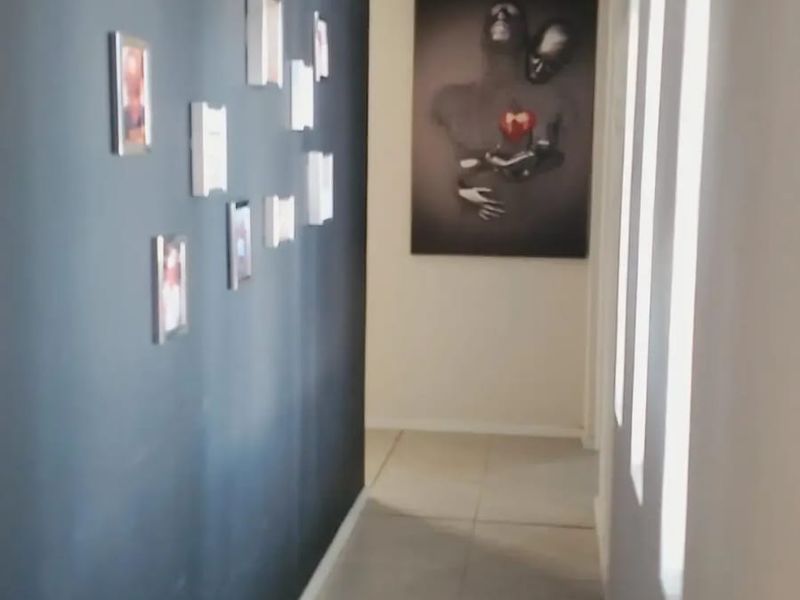 A bright, modern hallway featuring neutral tiled flooring and a striking dark accent wall, creating a clean and contemporary transition space.
