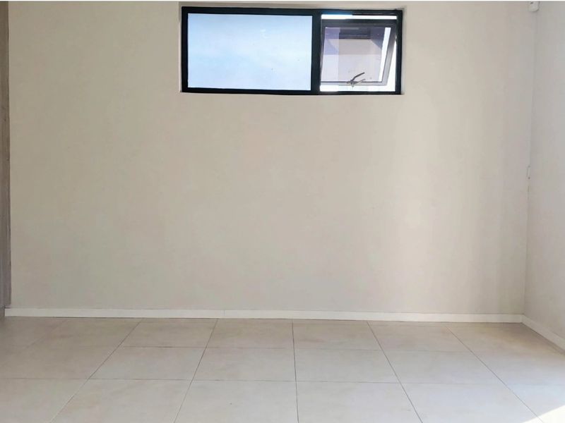 A bright, empty bedroom featuring neutral tiled flooring, built-in cupboards, and a sliding glass door providing access to the exterior.
