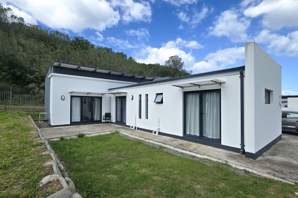 Rear view of a modern single-story home featuring a concrete patio, sliding glass doors, and a landscaped garden area against a hillside backdrop.