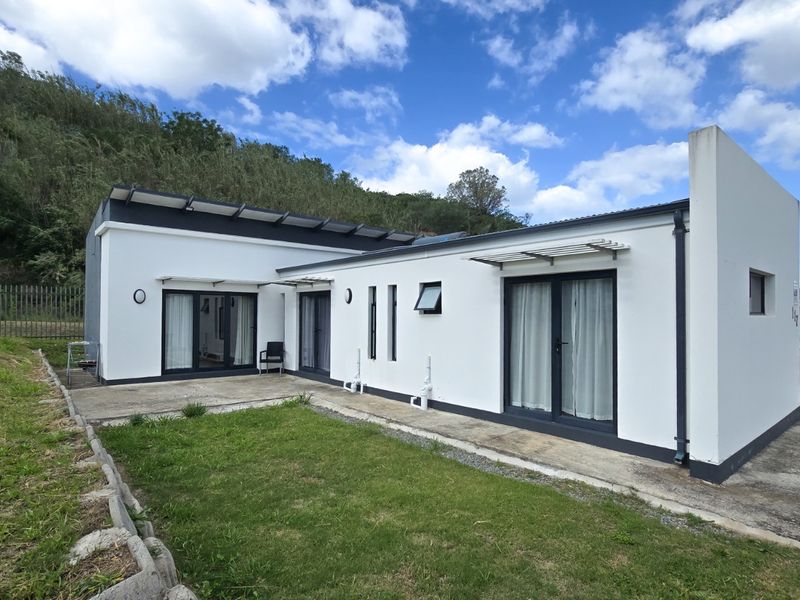 Rear view of a modern single-story home featuring a concrete patio, sliding glass doors, and a landscaped garden area against a hillside backdrop.