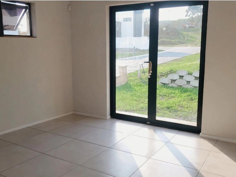 A bright, empty living area featuring neutral tiled flooring and large glass doors providing direct access to the garden.