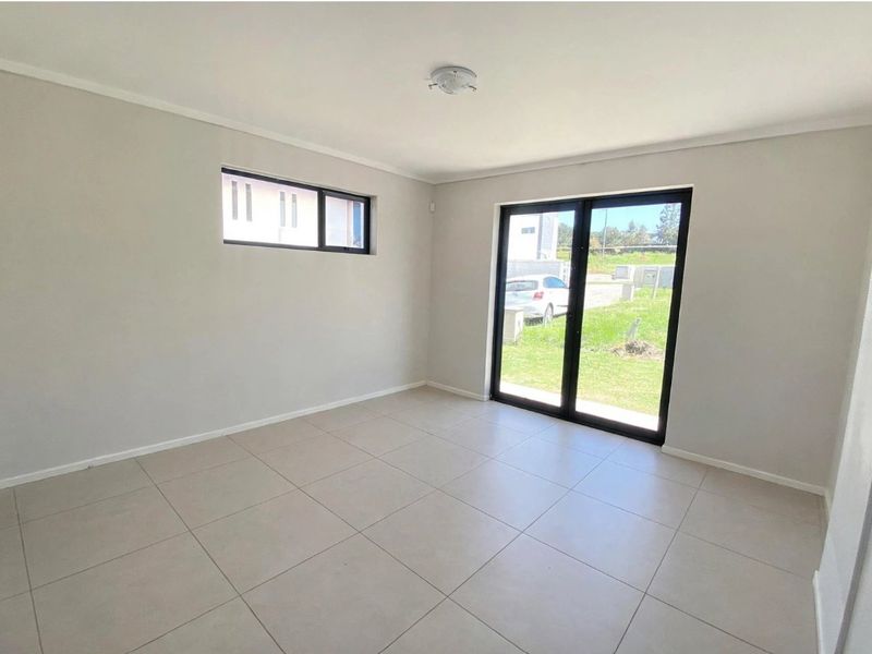 A bright, empty living room featuring neutral tiled flooring, modern aluminium sliding doors leading to the garden, and clean, well-maintained wall finishes.