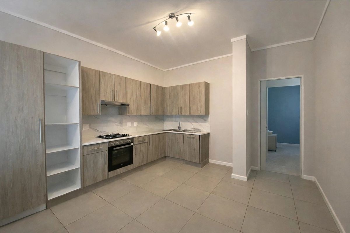 Modern kitchen featuring light wood-grain cabinetry, marble-look backsplash, gas hob, electric oven, and neutral tiled flooring in an open-plan layout.