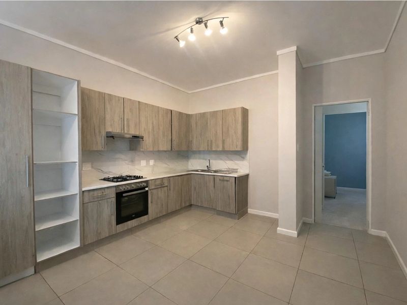 Modern kitchen featuring light wood-grain cabinetry, marble-look backsplash, gas hob, electric oven, and neutral tiled flooring in an open-plan layout.
