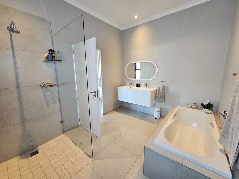 Modern bathroom featuring a spacious walk-in shower with glass screen, a sleek wall-mounted double vanity, and a built-in bathtub with neutral tiling.