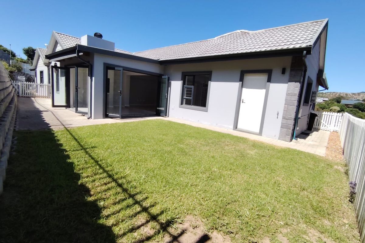 Rear view of the property featuring a well-maintained lawn, concrete patio area, and modern bi-fold doors leading into the home.