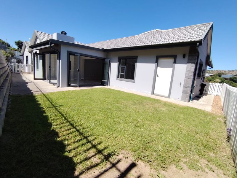 Rear view of the property featuring a well-maintained lawn, concrete patio area, and modern bi-fold doors leading into the home.