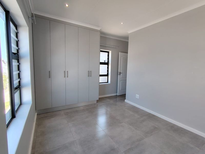 A bright, modern bedroom featuring neutral grey walls, large format floor tiles, and extensive built-in cupboard storage with contemporary finishes.