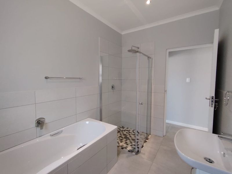 Modern bathroom featuring a built-in bathtub, separate glass-enclosed shower, and a pedestal washbasin with neutral tiled finishes.
