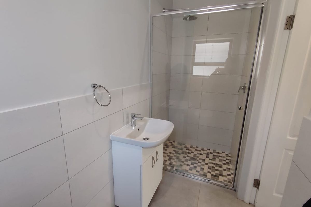 A clean, modern bathroom featuring a glass-enclosed shower with mosaic floor tiles and a white vanity basin with chrome fixtures.