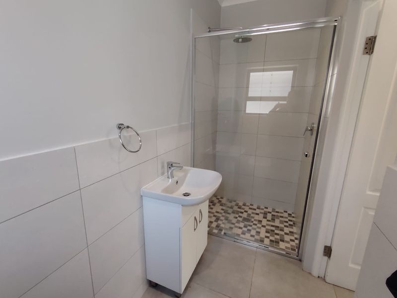 A clean, modern bathroom featuring a glass-enclosed shower with mosaic floor tiles and a white vanity basin with chrome fixtures.