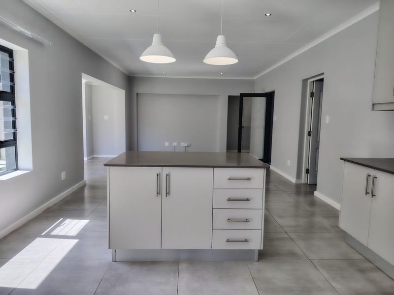 Modern open-plan kitchen area featuring a central island with stone countertops, sleek cabinetry, tiled flooring, and contemporary pendant lighting in a neutral color palette.