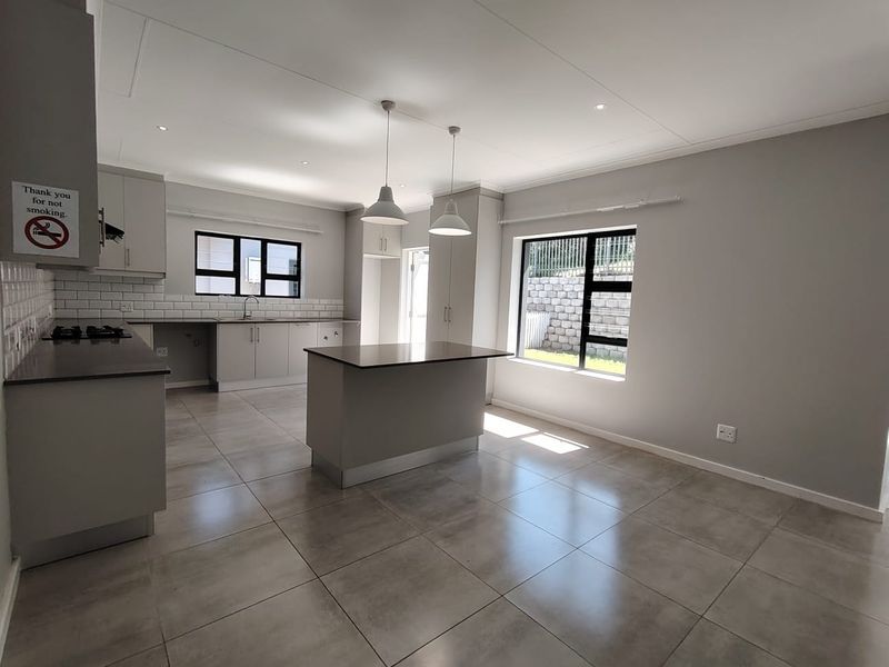 Modern open-plan kitchen featuring a central island, sleek cabinetry, gas hob, subway tile backsplash, and large windows providing ample natural light.