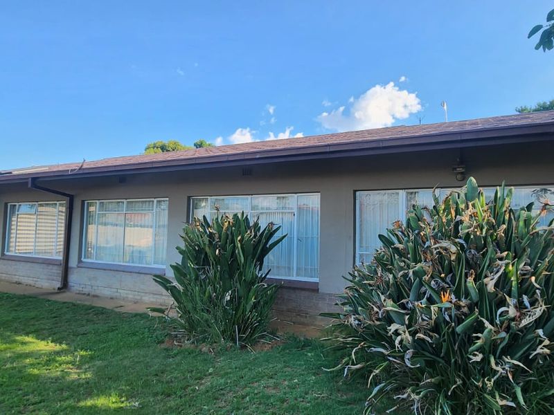 Rear elevation of the house featuring a tiled roof, large aluminium-framed windows, and an exterior air conditioning unit set against a lawned garden.
