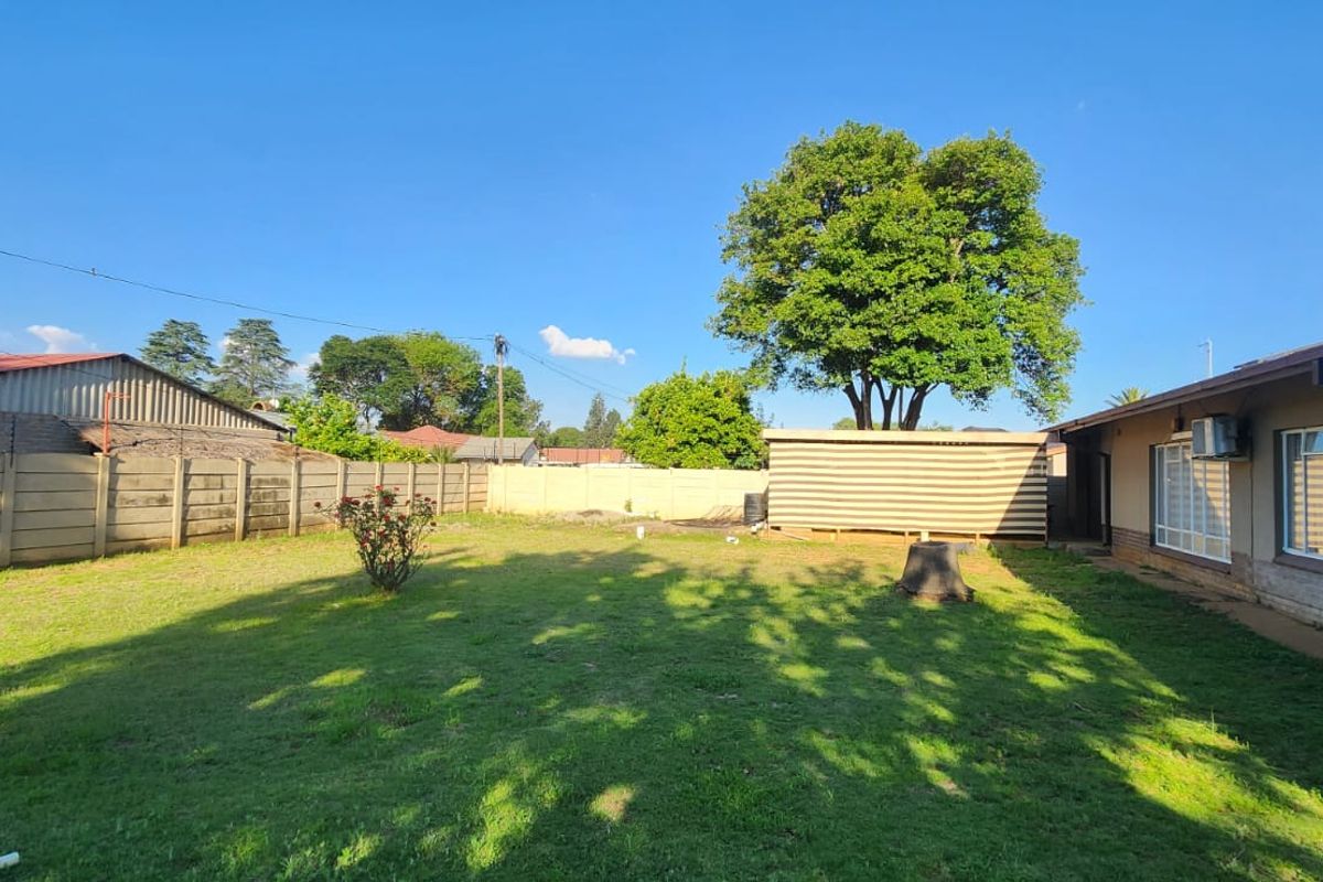 A spacious rear garden featuring a large lawn, precast concrete boundary walls, and exterior access to the main house structure.