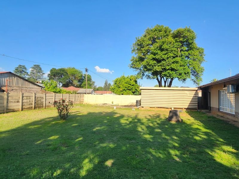 A spacious rear garden featuring a large lawn, precast concrete boundary walls, and exterior access to the main house structure.