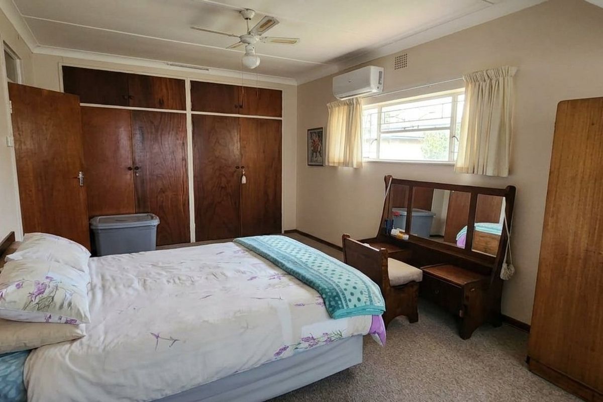 A functional bedroom featuring built-in wooden cupboards, a ceiling fan, and a wall-mounted air conditioning unit, offering a comfortable and practical living space.