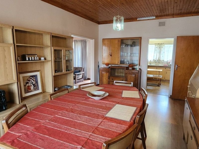 A traditional dining room featuring a timber-paneled ceiling, laminate flooring, and extensive built-in cabinetry, with an open transition to the adjacent kitchen area.