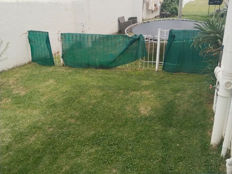 A private rear garden area featuring a lawn, perimeter wall with electric fencing, and external plumbing fixtures.