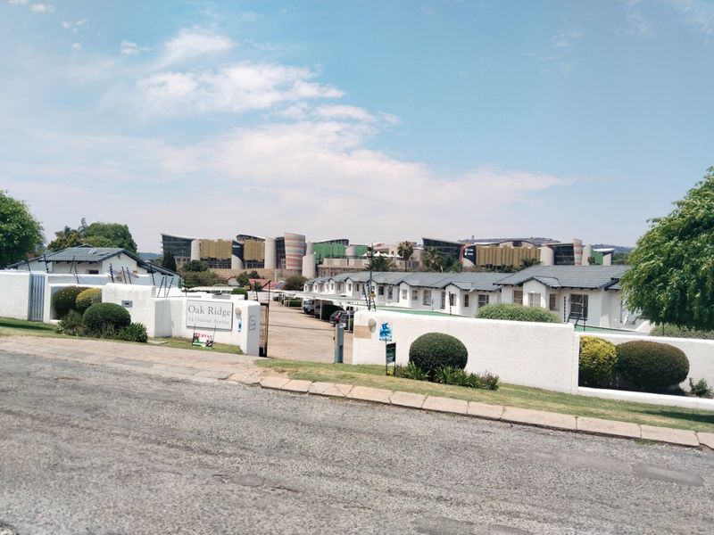Street view of the Oak Ridge apartment complex entrance, featuring a secure gated access point, perimeter walling with electric fencing, and paved driveway.