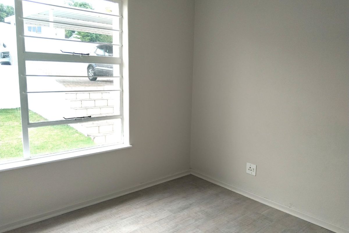 A bright, empty bedroom featuring modern laminate flooring, neutral wall tones, and a window fitted with security burglar bars.
