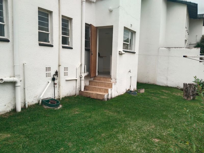 Rear exterior view of the apartment featuring tiled entrance steps, external plumbing, and a small private garden area.