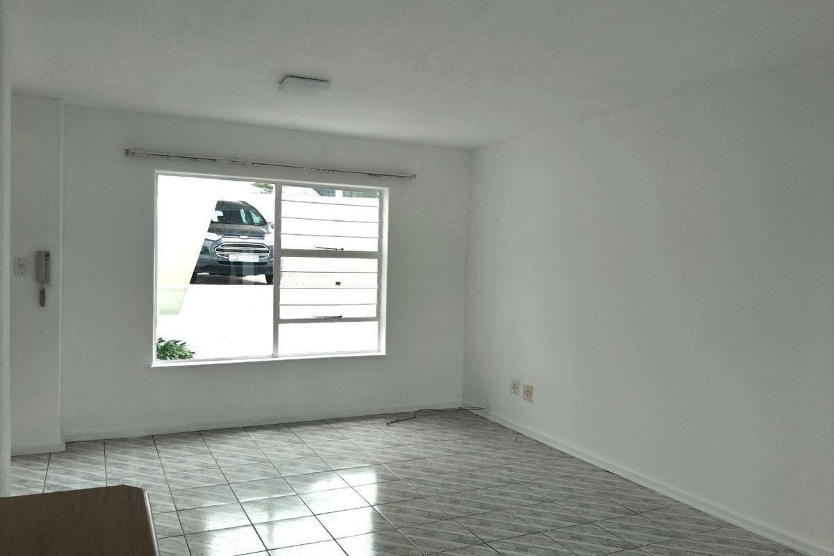 A bright, empty living room featuring neutral tiled flooring and a large window, providing a clean canvas for interior design.