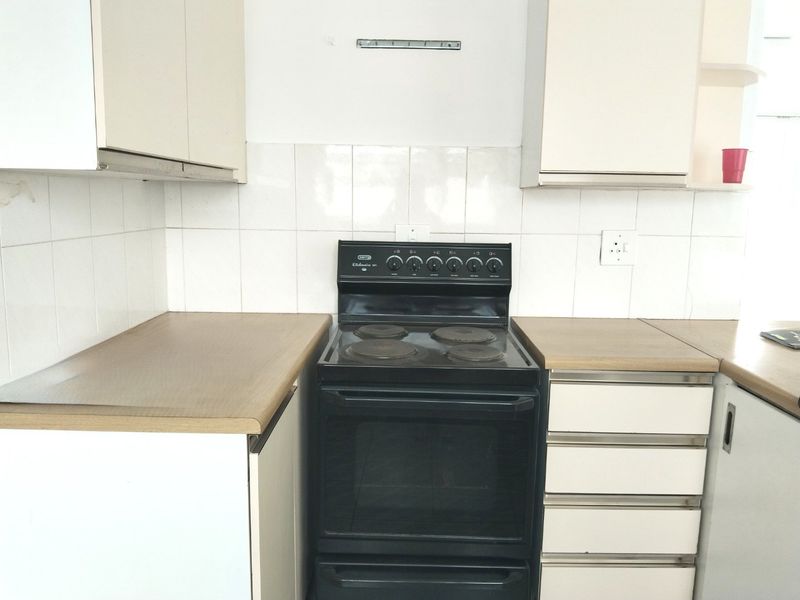 A dated kitchen featuring white cabinetry, laminate countertops, and a black electric stove with a tiled backsplash.