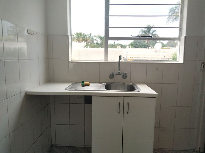 A functional scullery area featuring a stainless steel sink, built-in base cabinetry, and tiled splashbacks, positioned beneath a window with security bars.