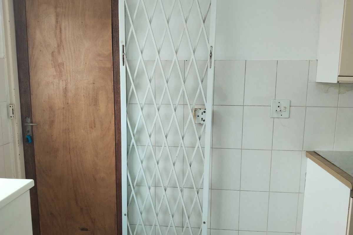 A kitchen area featuring a security gate, tiled splashback, and built-in cabinetry, showing signs of wear and requiring minor maintenance.