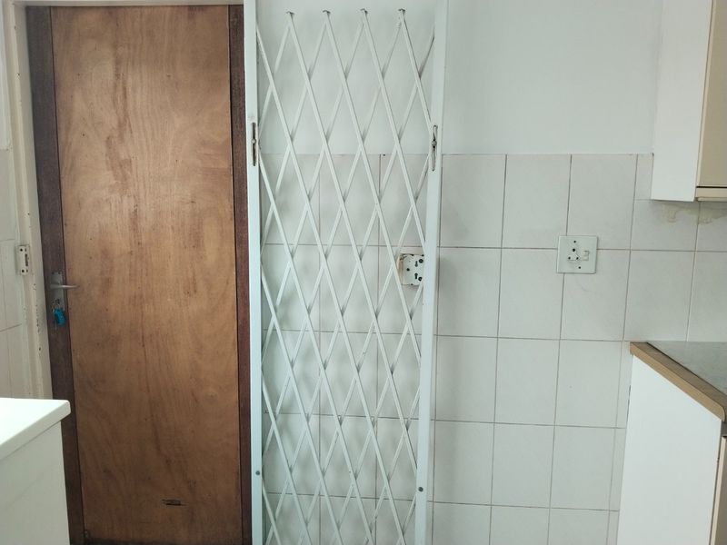 A kitchen area featuring a security gate, tiled splashback, and built-in cabinetry, showing signs of wear and requiring minor maintenance.
