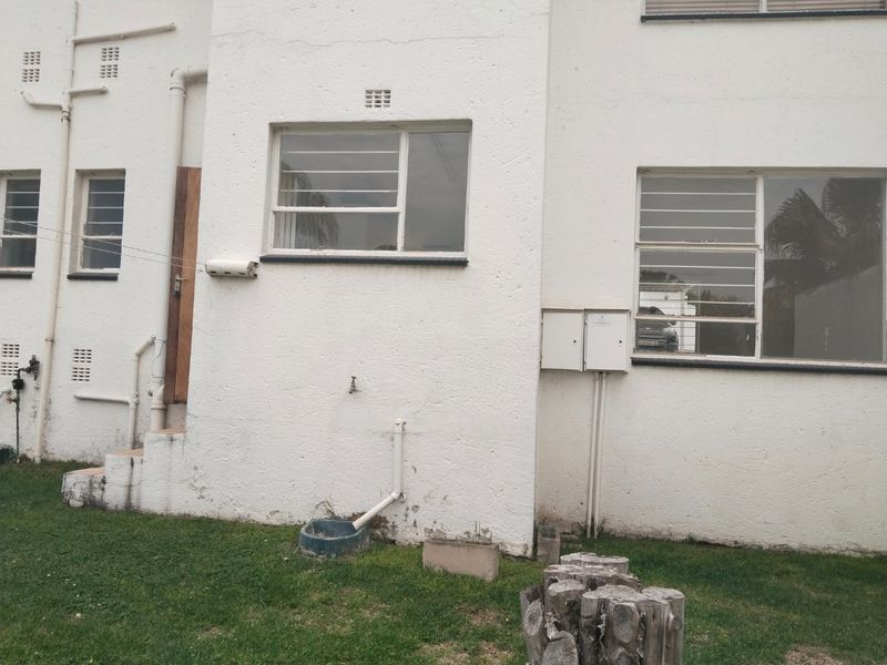 Rear exterior view of the apartment building featuring white textured walls, security bars on windows, and external utility plumbing.