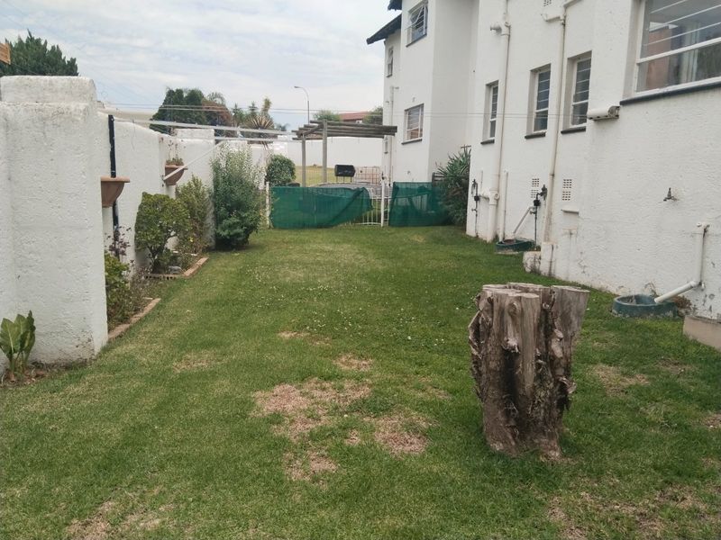 A rear garden area featuring a lawn, boundary wall, and pergola, showing signs of wear and maintenance requirements.
