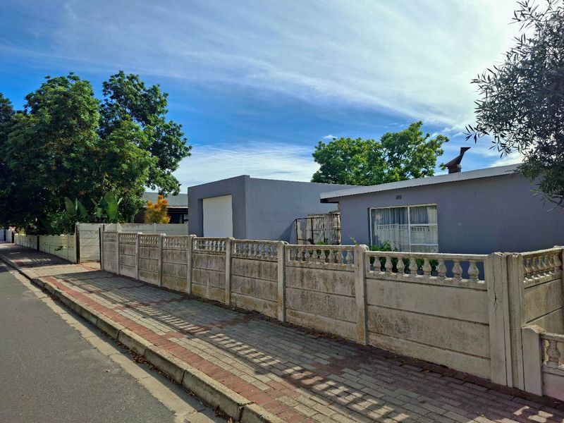 Street view of the property featuring a precast concrete boundary wall, paved sidewalk, and the front facade of the house with an attached garage.