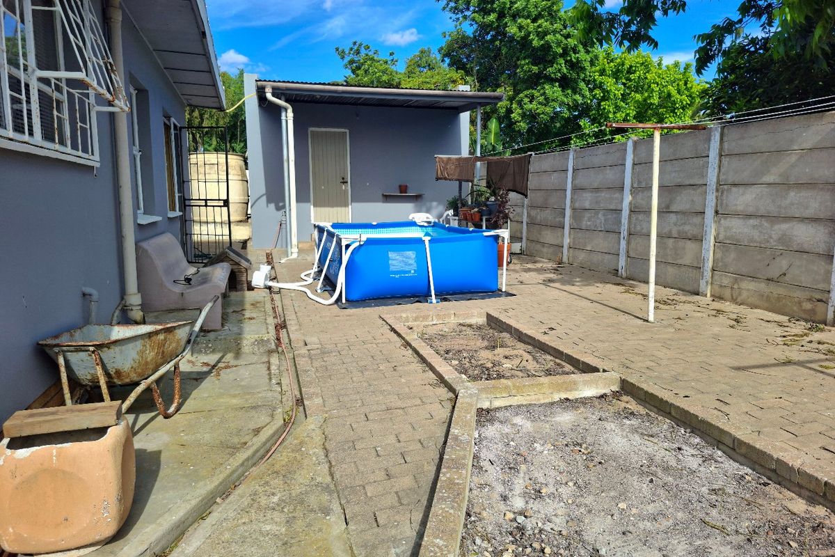 Rear exterior area featuring paved patio space, raised garden beds, a precast boundary wall, and a detached outbuilding.
