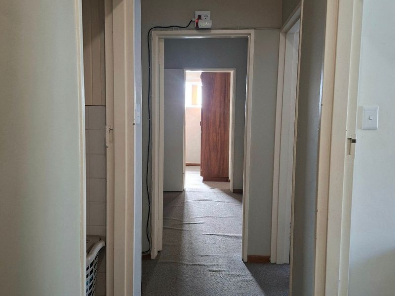 A narrow residential hallway featuring carpet flooring and multiple doorways leading to adjacent rooms, showing signs of wear and exposed surface wiring.