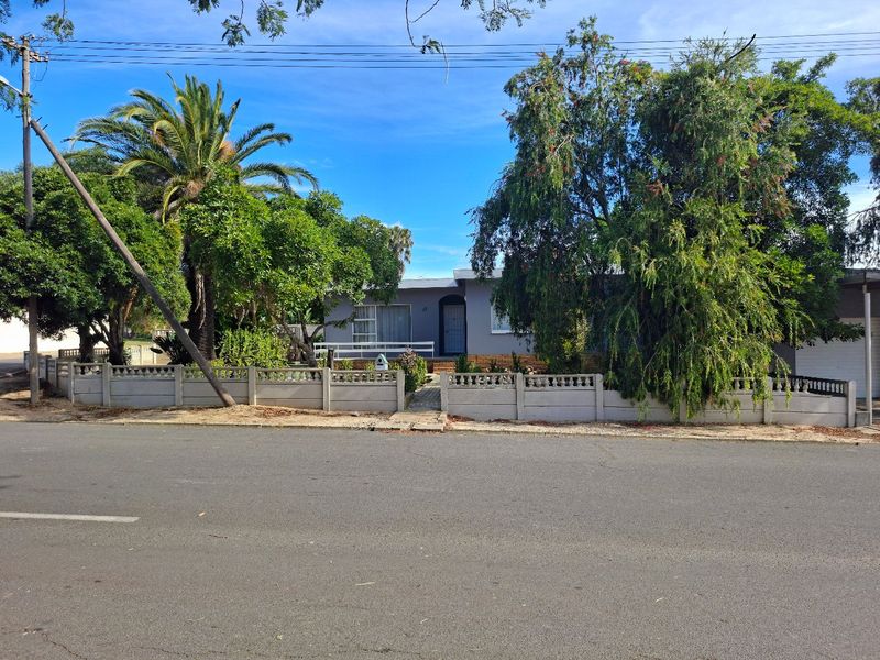 Front view of a single-story residential property featuring a precast concrete boundary wall, paved entrance path, and established garden landscaping.