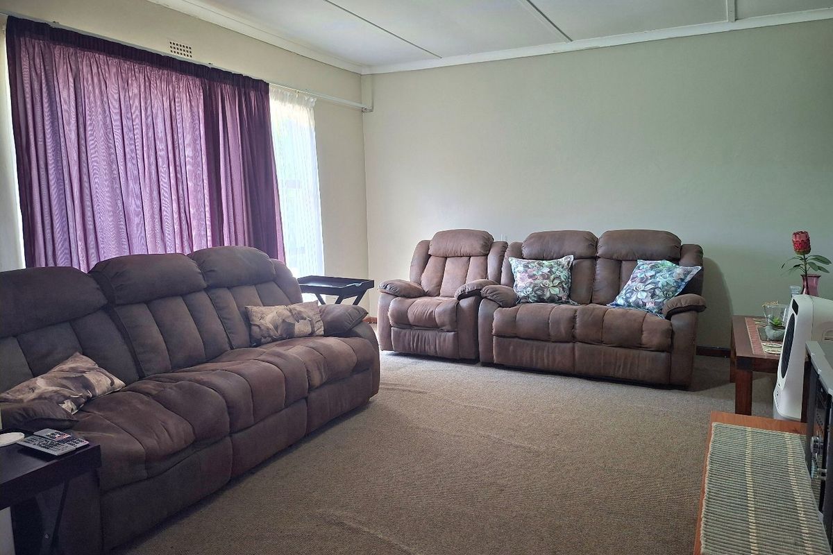 A spacious living room featuring neutral wall tones, carpeted flooring, and large windows with curtain tracks.