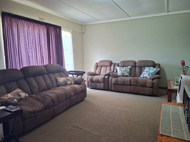 A spacious living room featuring neutral wall tones, carpeted flooring, and large windows with curtain tracks.