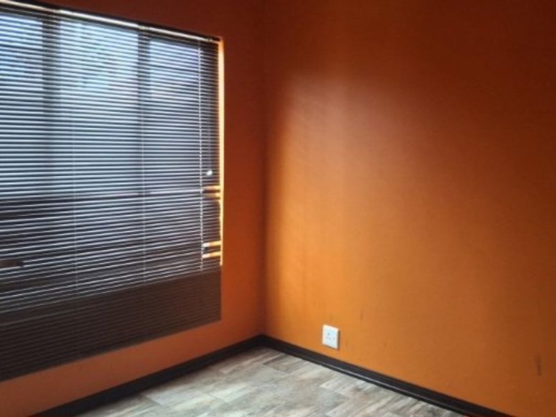 An empty bedroom featuring orange painted walls, wood-look flooring, and damaged venetian blinds over the window.
