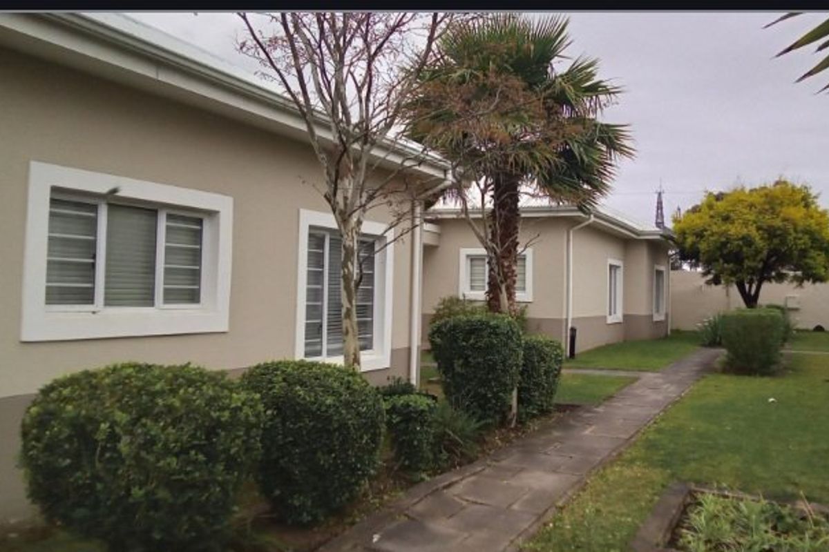 A view of the rear exterior of the townhouse, featuring a paved walkway, established garden, and security bars on the windows.